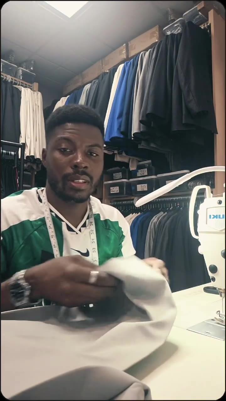 The DXA STITCH tailor with a tape measure in the workroom, racks of suits and uniforms behind him
